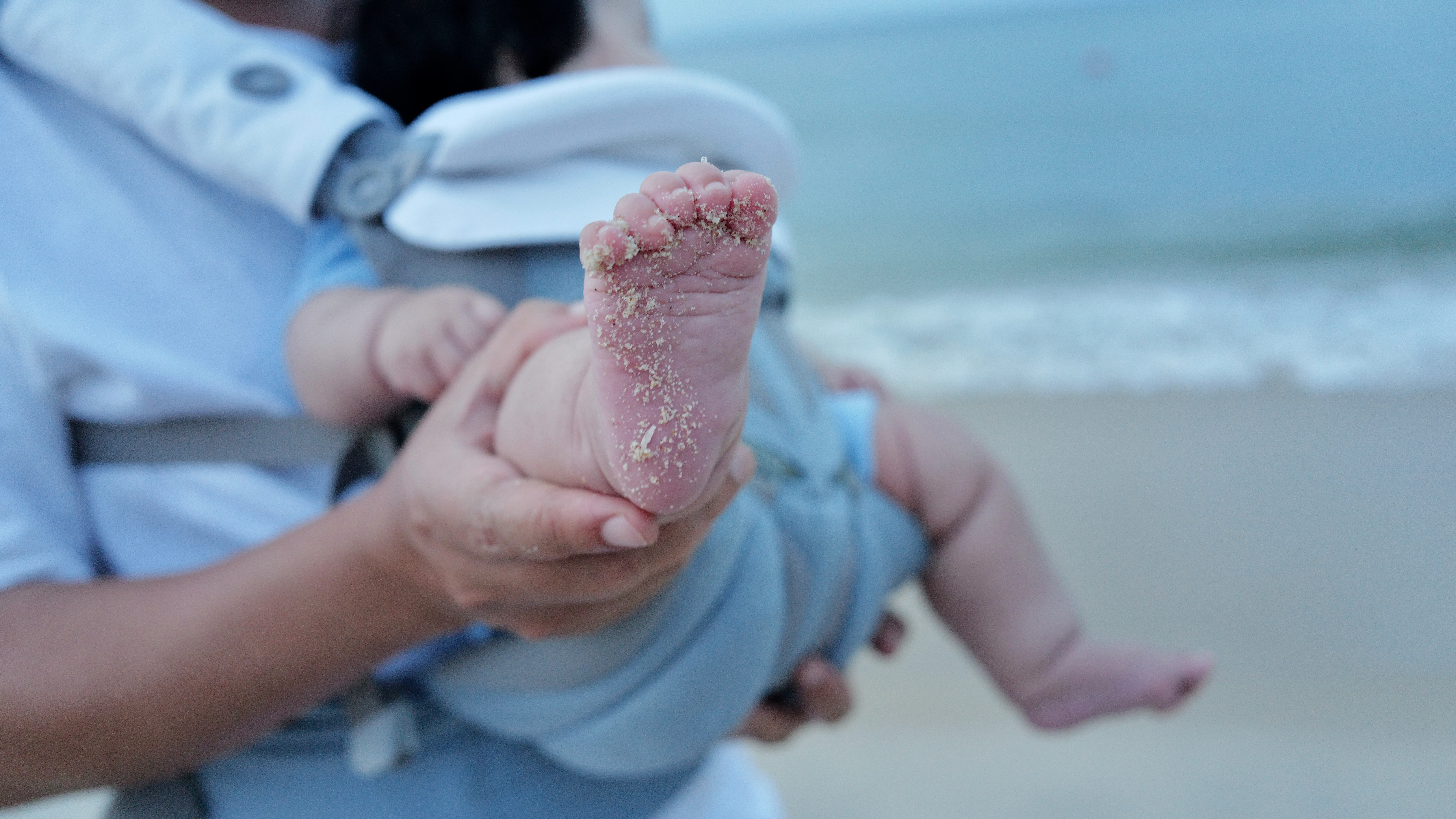 Bàn chân TiA phủ cát, được người lớn nâng đỡ trên bãi biển